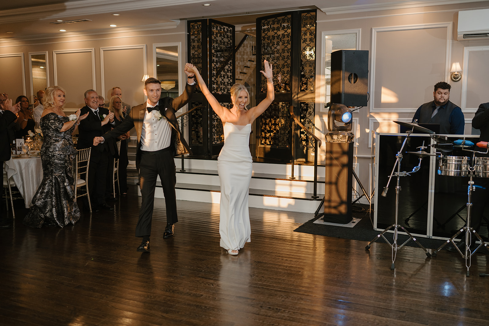 Newlyweds make a high-energy grand entrance into their wedding reception, cheering with guests applauding.